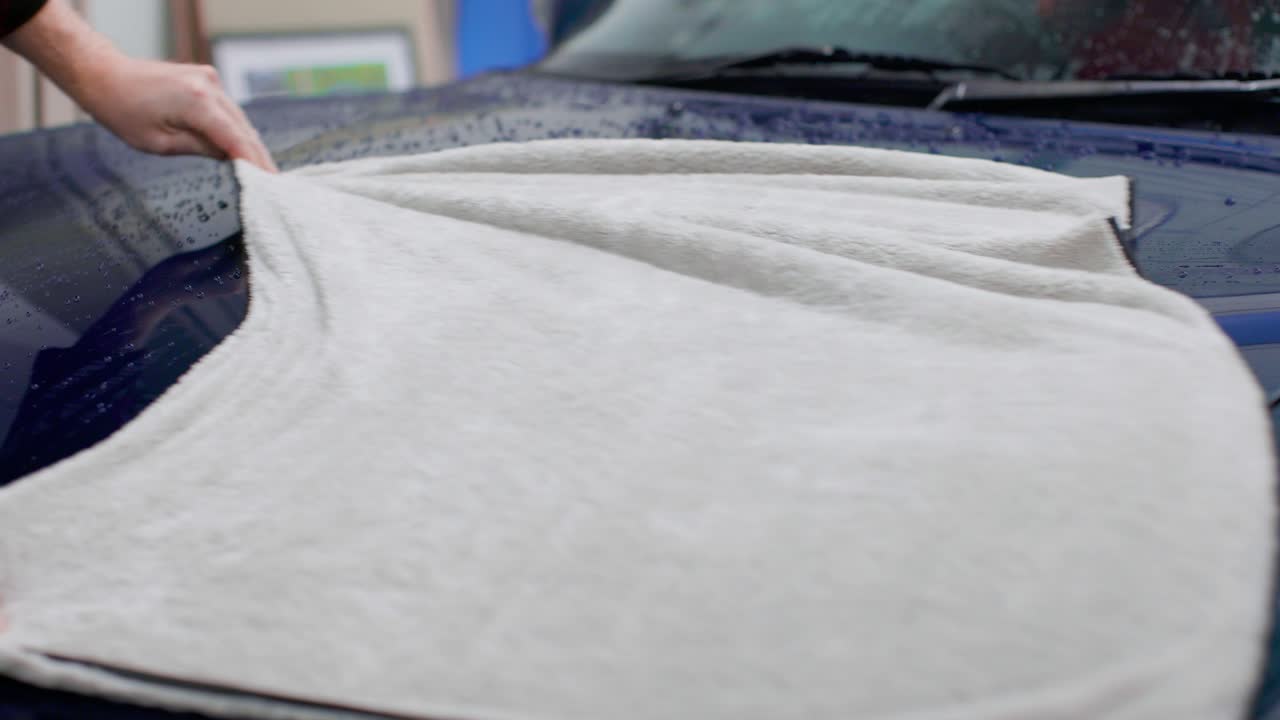 Wiping off the hood to dry a blue car after washing with big microfiber towel. Static shot in 4k.