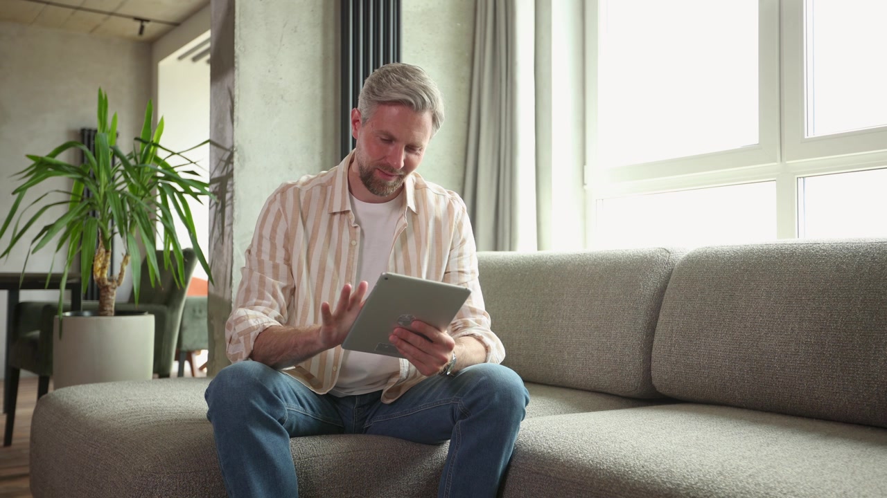 Smiling Man Using Digital Tablet on Couch at Home
