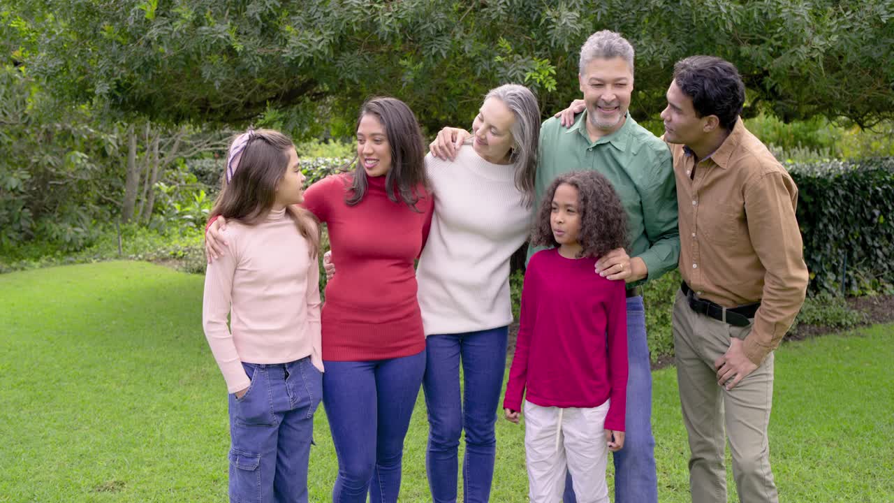 Diverse family draping arms responding to father raising arm and laughing together in garden