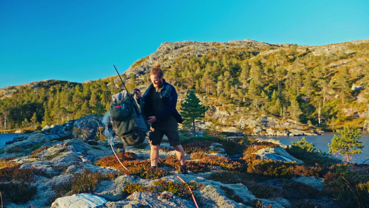 Un uomo sta facendo trekking su terreno roccioso con uno zaino, accompagnato da un cane, in un paesaggio montano all'aperto - Piano medio.