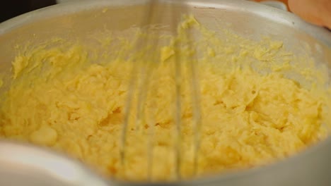 mashing cassava in a big mixing bowl with a whisk - yuca harvested from organic farms in the amazon rainforest