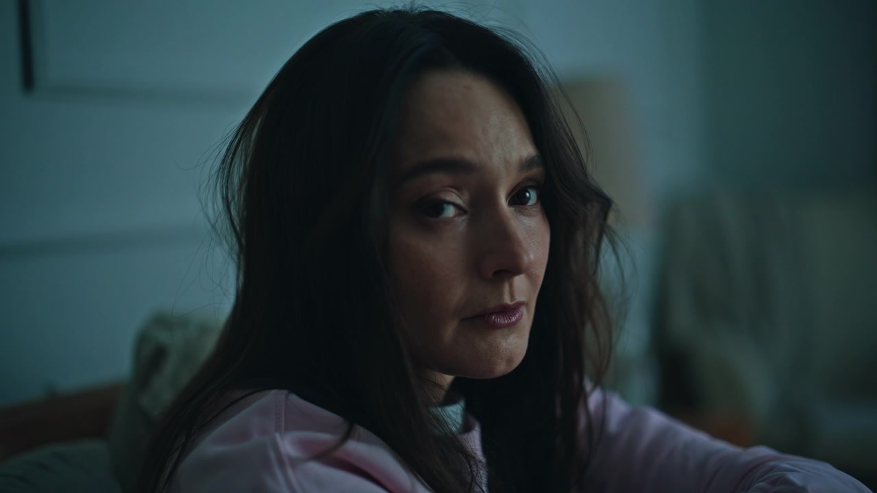 Unhappy lady sitting bed with pensive look at evening closeup. Emotionless woman