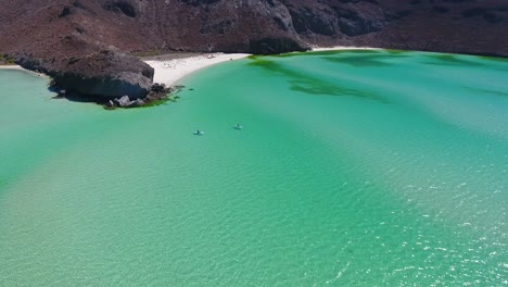 fast drone flight over and past two girls playing on paddleboards in clear turquoise water