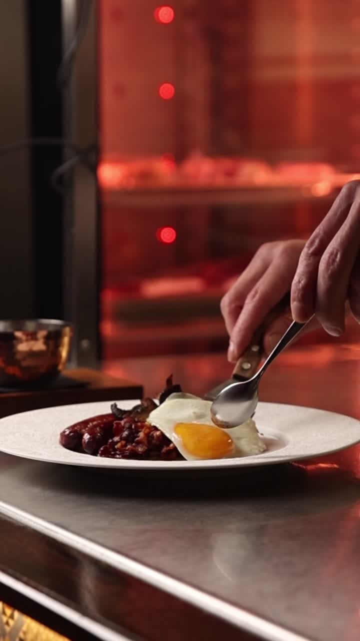 Chef Plating a Fried Egg with Sausages and Beans in a Restaurant Kitchen