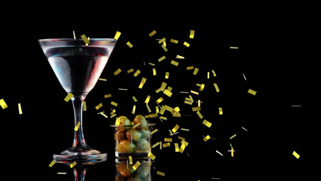 Golden-confetti-falling-over-cocktail-glass-and-olives-against-black-background