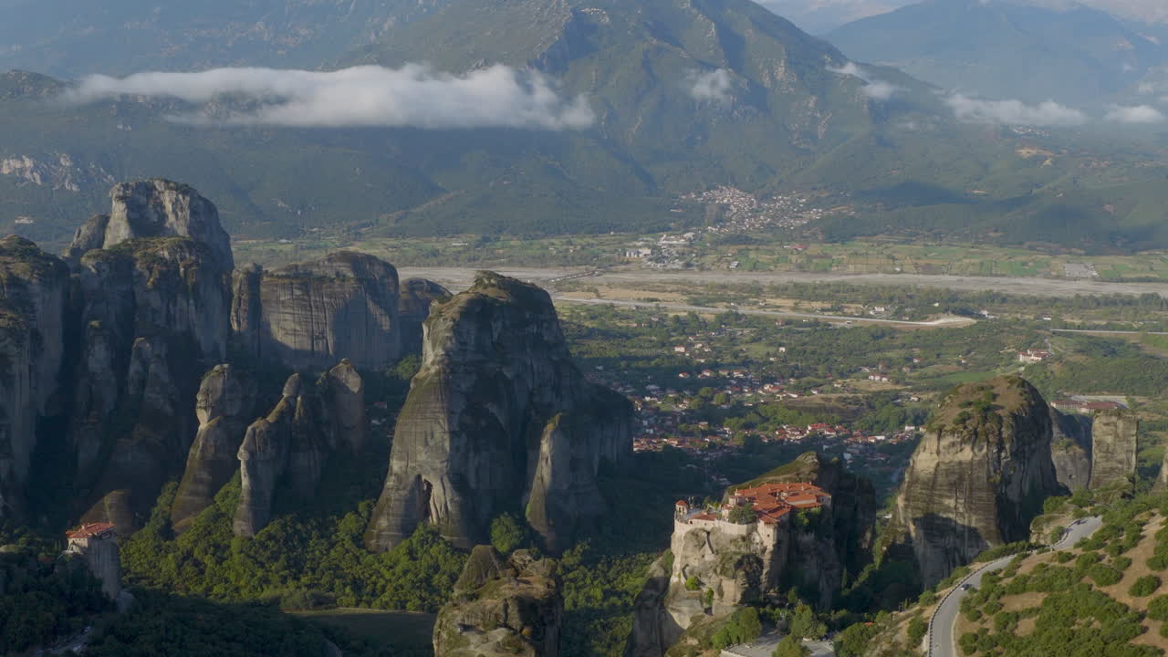Cinematic aerial view of Meteora monastery in Greece perched on towering cliffs, dramatic rock formations and lush green valley create a breathtaking historic scene