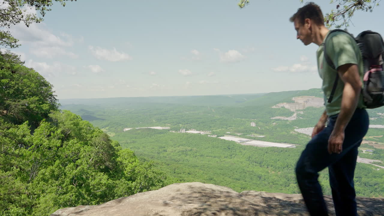 Hiker reaching mountain summit and sits down on rock to look at the amazing view from the top. Long hike up the hill backpacker stops for a break to rest and relax and look at nature scenery