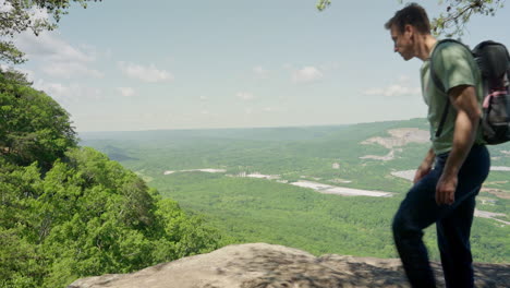 hiker reaching mountain summit and sits down on rock to look at the amazing view from the top. long hike up the hill backpacker stops for a break to rest and relax and look at nature scenery