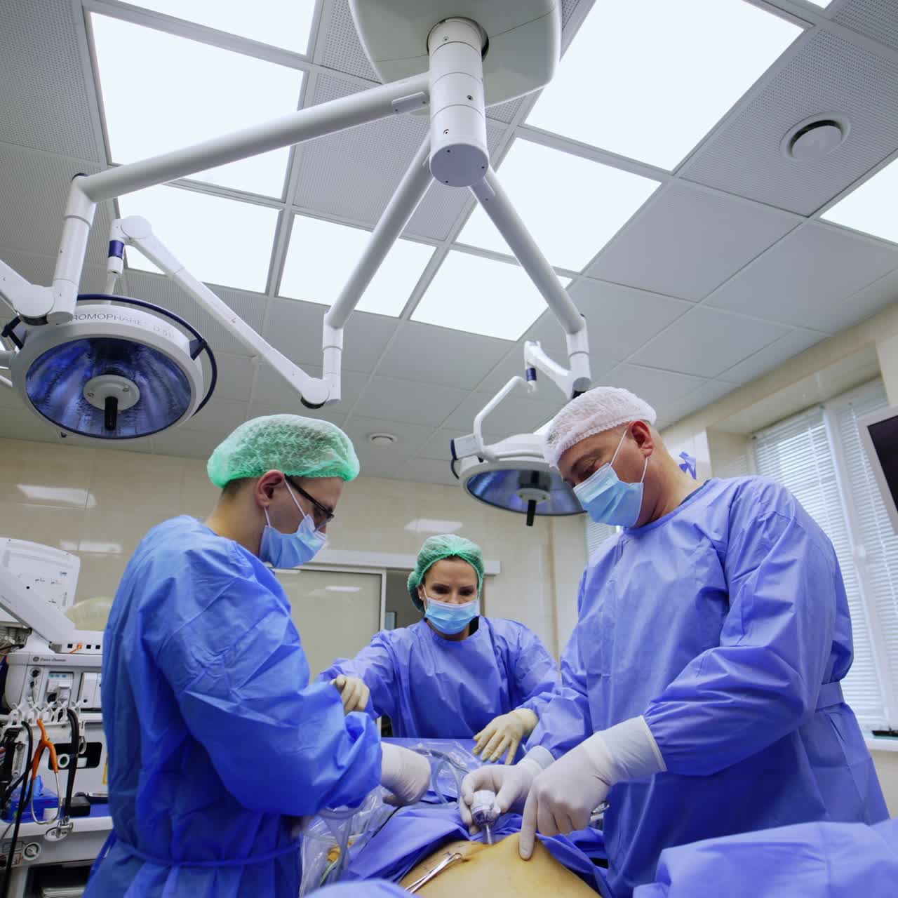 Older and younger surgeons working in modern surgery room. Doctors perform laparoscopy assisted by female nurse