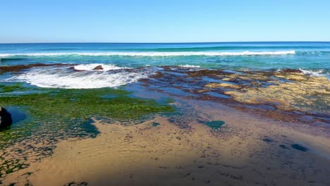 Waves-crashing-onto-a-rocky-beach-covered-with-green-seaweed