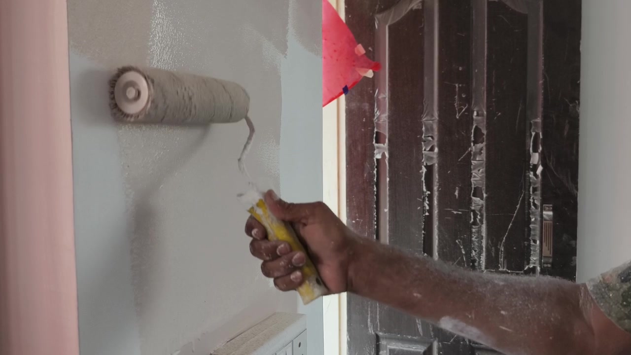 Close up of a mans hand using a paint roller to apply fresh white paint onto an indoor wall during a home renovation project in India.