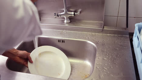 kitchen porter cleaning plates in sink