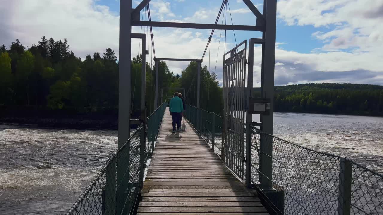 Bellissima vista di un fiume calmo circondato da una vegetazione lussureggiante con persone che camminano sul ponte sopra di esso