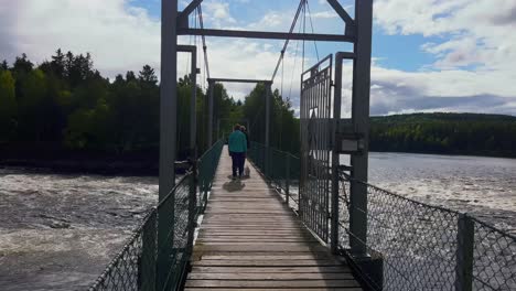 Schöne-Aussicht-Auf-Einen-Ruhigen-Fluss,-Umgeben-Von-üppigem-Grün,-Mit-Menschen,-Die-Auf-Der-Brücke-Darüber-Laufen