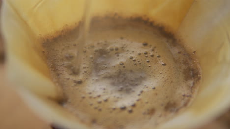 up close macro view of fresh, ground coffee beans in chemex filter paper having hot water poured over for morning coffee