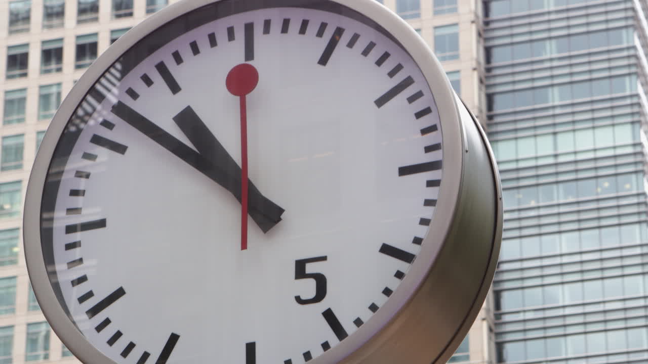 A striking close-up of a large clock at Canary Wharf, set against the backdrop of modern skyscrapers. The composition emphasizes time's role in the bustling urban landscape
