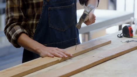 female welder hammering nail on a wooden plank 4k