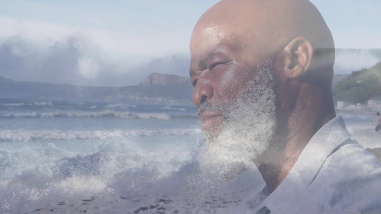 Transizione in dissolvenza che mostra un uomo seduto che emerge di profilo sulla spiaggia, si gira, chiude gli occhi, mostrando calma.