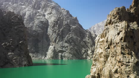 Aerial-shot-of-the-Kel-Suu-lake-in-Kyrgyzstan,-flying-past-the-rocky-mountain-cliffs