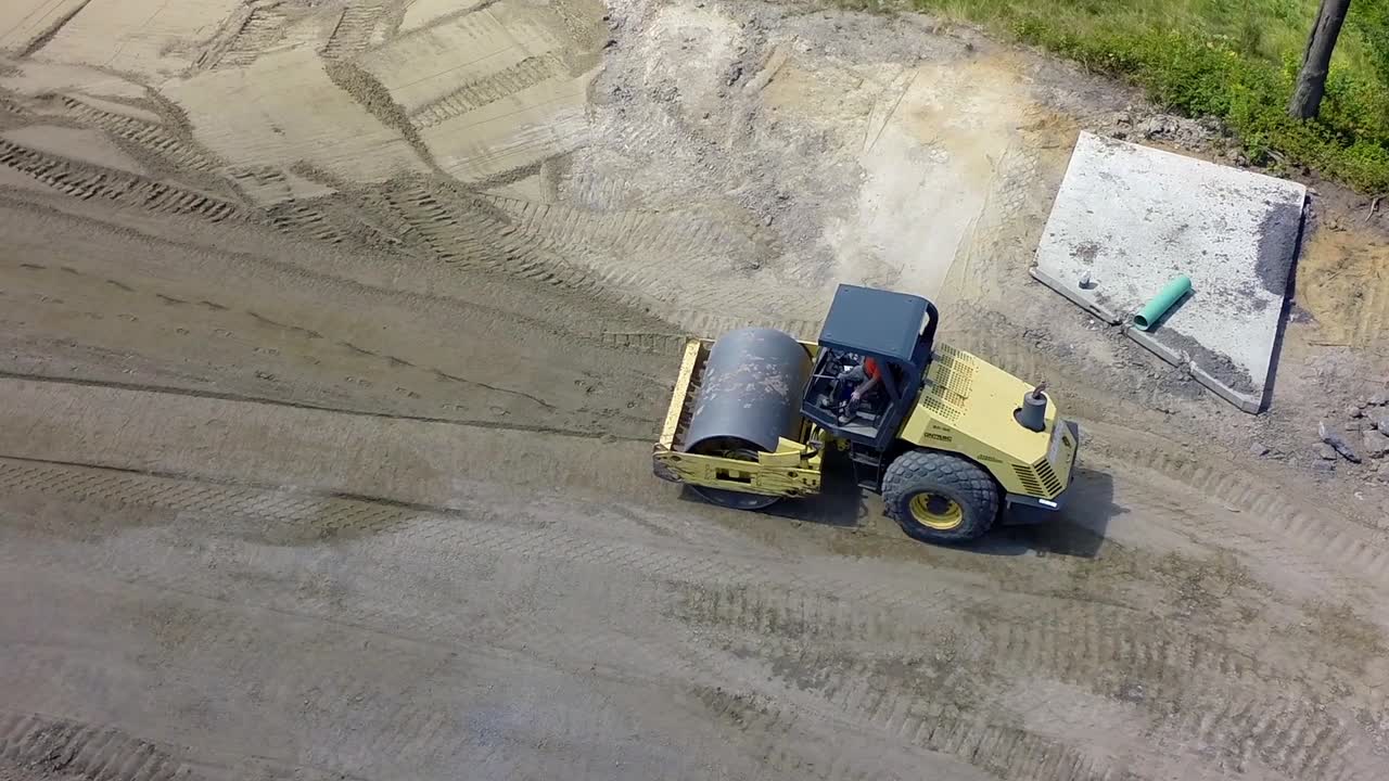 Heavy roller flattens a dirt road as drone follows overhead