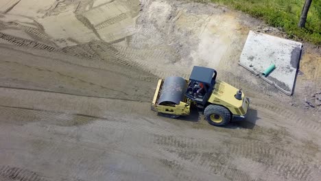 heavy roller flattens a dirt road as drone follows overhead