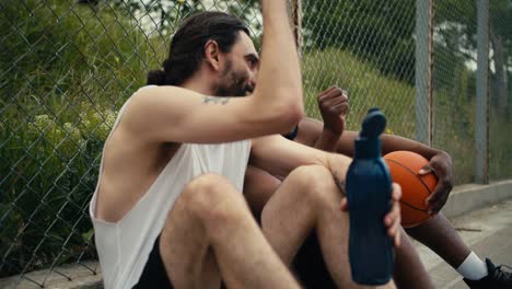 un hombre con una camiseta blanca y un hombre de piel negra que sostiene una pelota de baloncesto en sus manos están hablando de baloncesto en la cancha de baloncesto