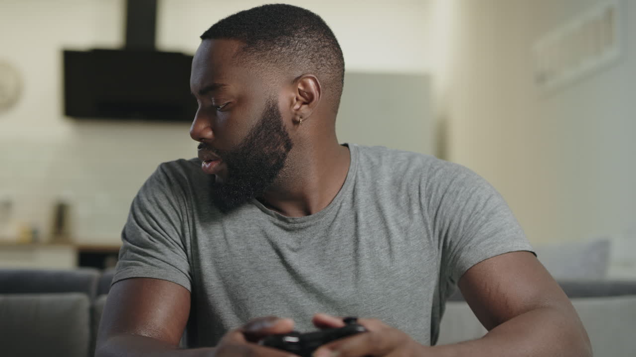 Koncentreret mand spiller spil i køkkenet. Frustreret fyr holder PlayStation.