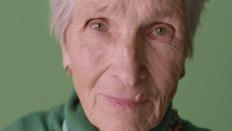 Close-Up-View-Of-Blonde-Senior-Woman-With-Short-Hair-Wearing-Green-Sweater-Posing-On-Green-Background-Looking-At-Camera