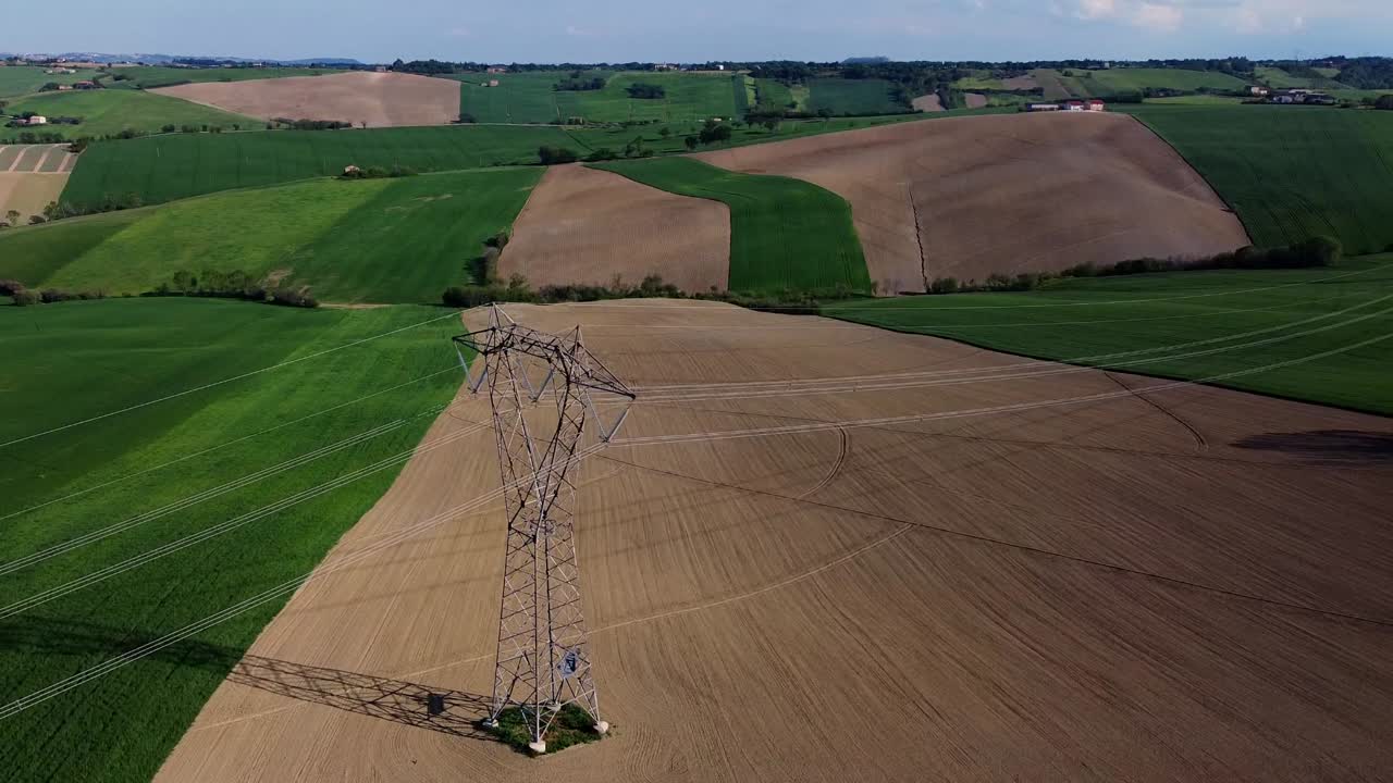 rural landscape with high voltage wires and pylons in the middle of cultivated fields, orbit shot