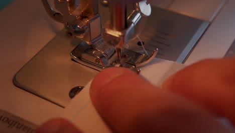 Close-up-of-slow-moving-needle-of-sewing-machine-and-fingers-of-operator-pulling-fabric-through