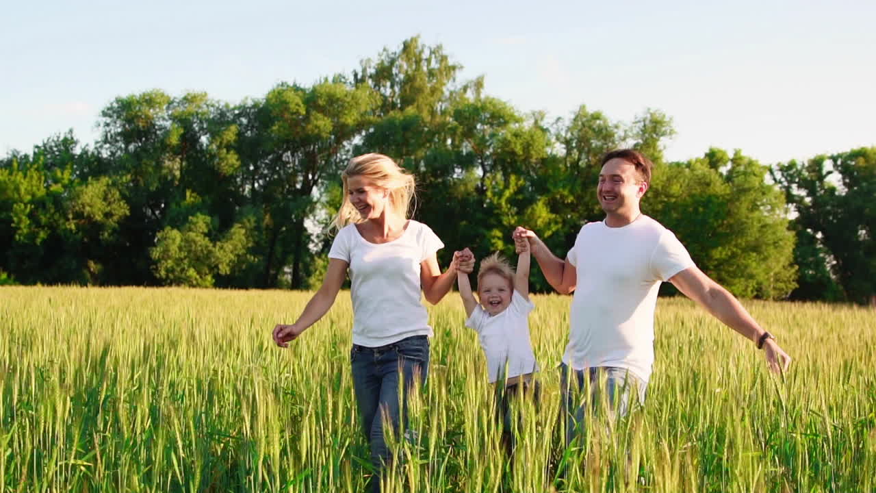 familia feliz: padre, madre e hijo, corriendo en el campo vestidos con camisetas blancas