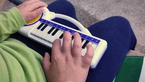 a child is sitting outside on a bench and learning to play the toy piano keyboard. close-up shot