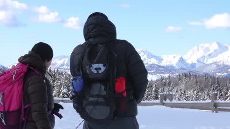 Two-Hikers-Looking-and-Pointing-at-Snowy-Mountains-in-Winter-on-a-Sunny-day