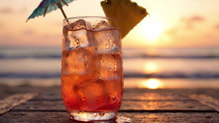 A Refreshing Sunset Drink: A Close-Up of a Colorful Cocktail Glass with Ice, Garnished with a Pineapple Slice and an Umbrella Against a Beautiful Beach Sunset.