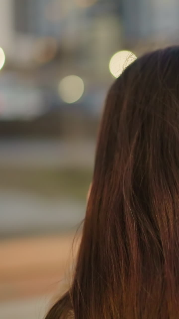 A close-up back shot of a woman with long brown hair, set against a softly blurred urban background. quiet elegance of the scene, focusing on the texture and color of the hair