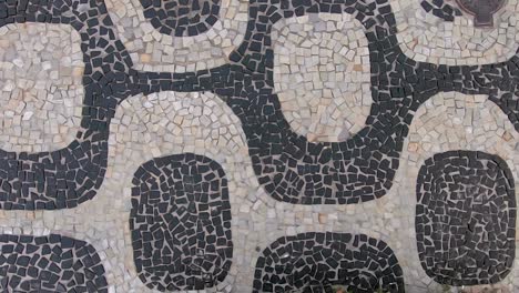 slow motion sideways moving top down closeup view of the so called portuguese pavement design in ipanema, rio de janeiro, with typical shapes on the beach boulevard sidewalk