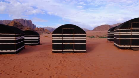 Tourism-Arabian-Bedouin-tents-in-vast,-remote-Wadi-Rum-desert-landscape-in-Jordan-with-bright-red-sand-and-blue-skies