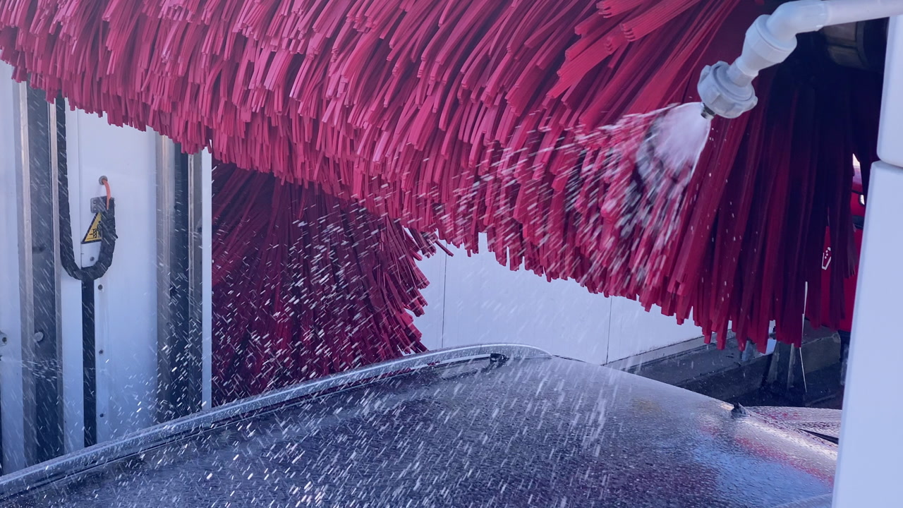 Automatic car wash with spinning red brushes and water spraying onto a car, providing efficient vehicle cleaning service