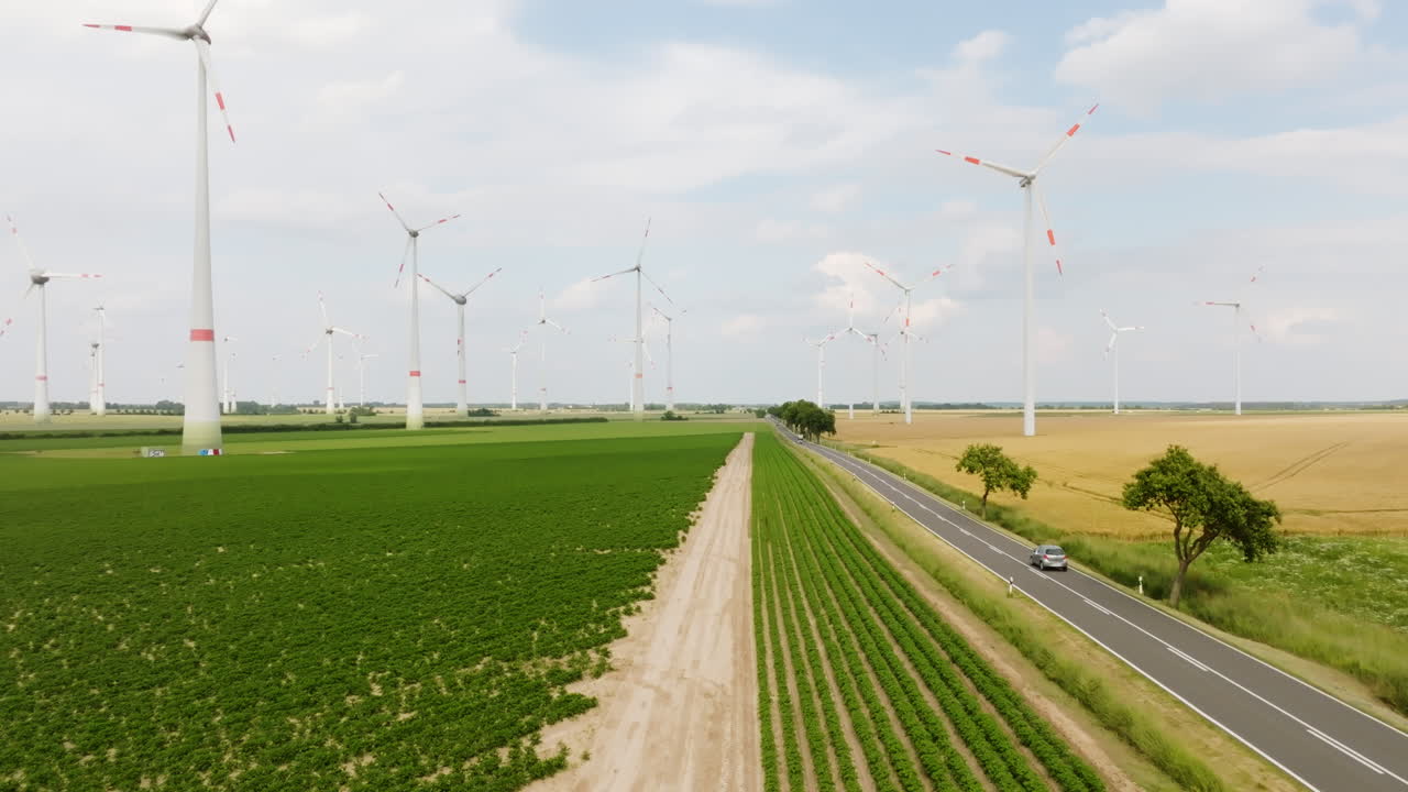 Drone flying low over farmlands, traffic on a road in middle of Eolic farm