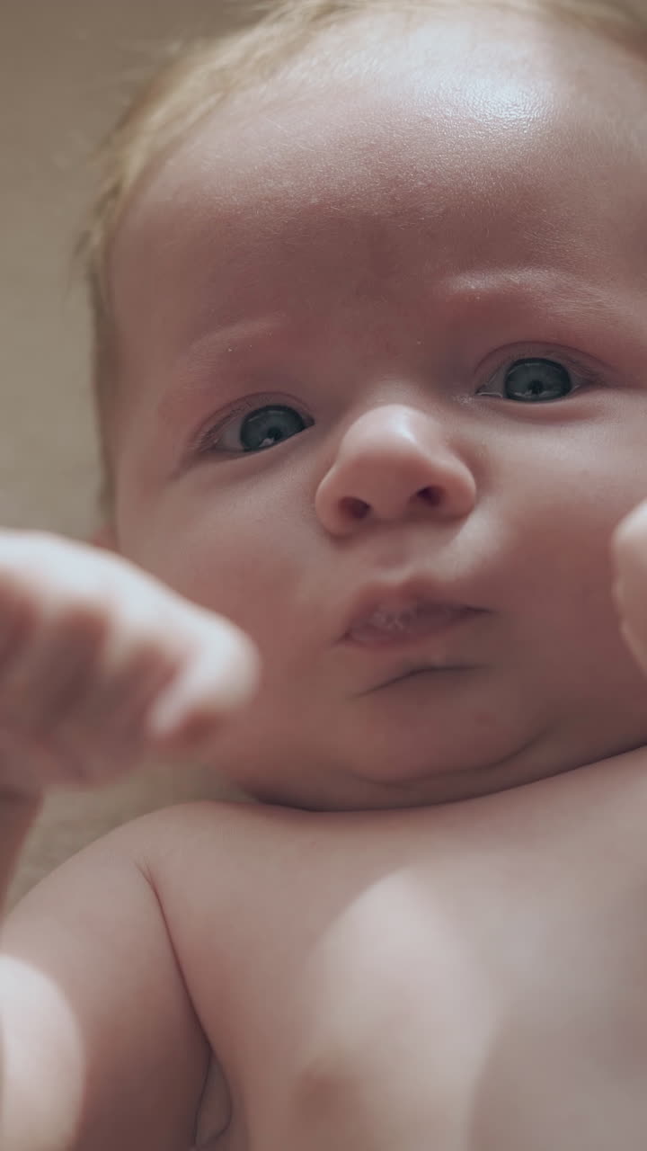 adorable newborn son with short fair hair and large blue eyes lies on changing table and moves hands extreme close view