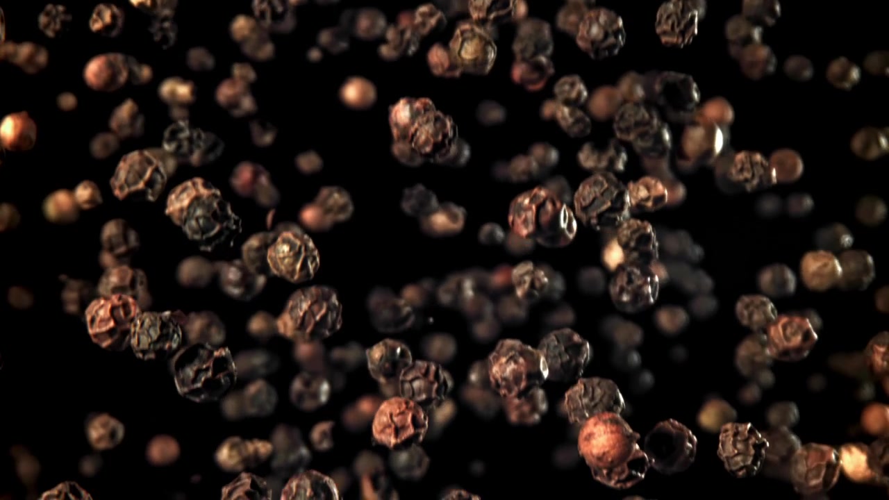 Svarte pepperkorn som faller i super sakte film på svart bakgrunn