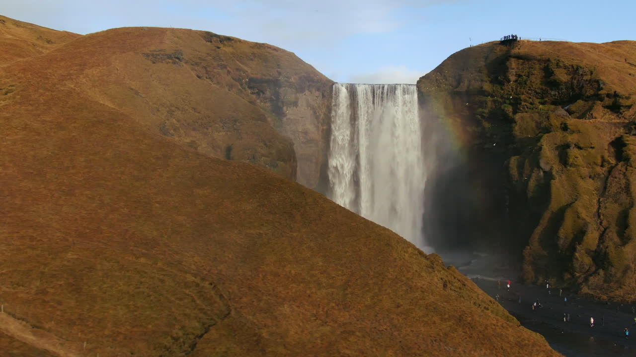 drone cinematográfico skogafoss cascada islandia panorámica zoom a la derecha con los pájaros, el arco iris y la luz del sol de la tarde