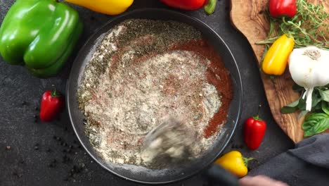 making a vibrant cajun spice blend, mixing red paprika, cayenne pepper, oregano, thyme, white garlic onion powder and black pepper in a bowl, creating a striking contrast against a black background.