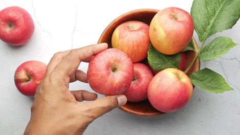 la mano recogiendo una manzana roja de un cuenco de madera