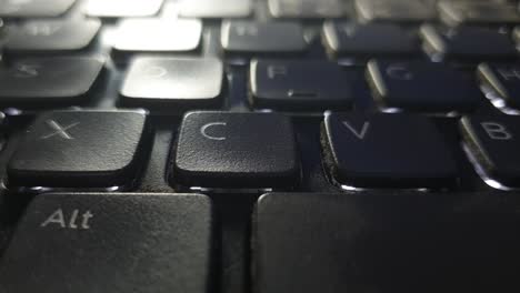 teclado retroiluminado de portátil sucio y roto con suciedad y polvo y la punta del dedo moviéndose sobre teclas desgastadas
