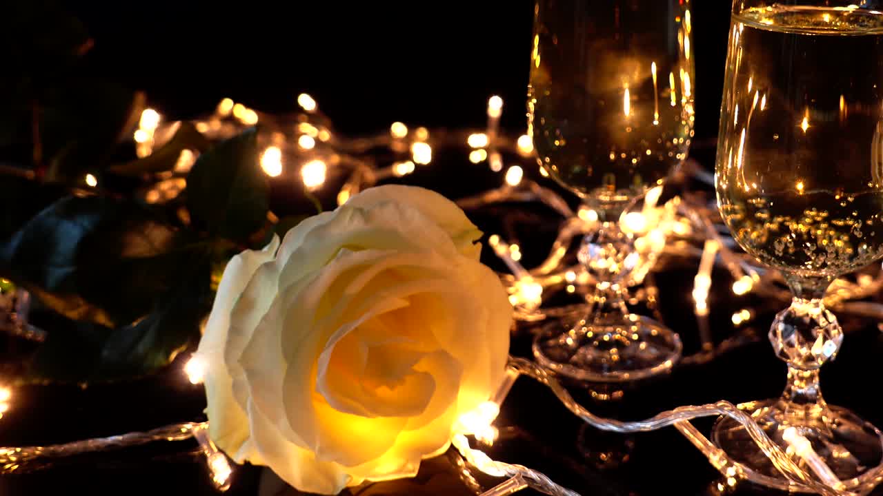 Calici da champagne e una rosa sullo sfondo di ghirlande luminose