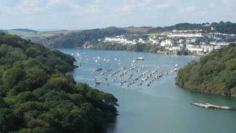 wide rising aerial reveal over the river fowey, to reveal the dramatic cornish coastline and the towns of fowey and polruan, uk