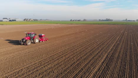 moving drone shot of red tractor plowing a brown, earthy farmland with birds, seagulls following, flying