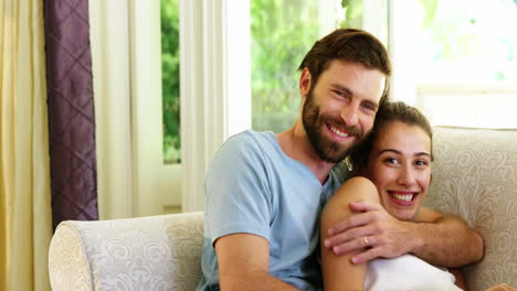 una pareja linda sentada en un sofá con una computadora portátil y abrazándose