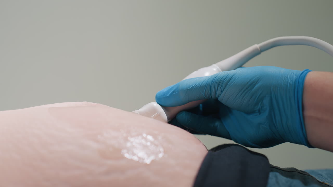 radiologist applies transducer on tummy of pregnant woman using scanning gel while patient reacts slightly to abdominal movement during ultrasound scan showing detailed close up of diagnostic process